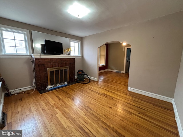 unfurnished living room featuring a brick fireplace, arched walkways, light wood-type flooring, and baseboards