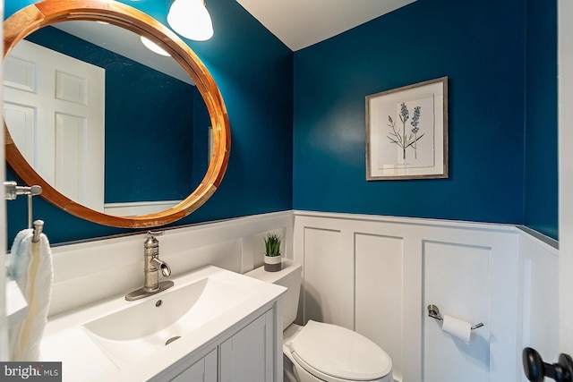 bathroom with vanity, a decorative wall, toilet, and a wainscoted wall