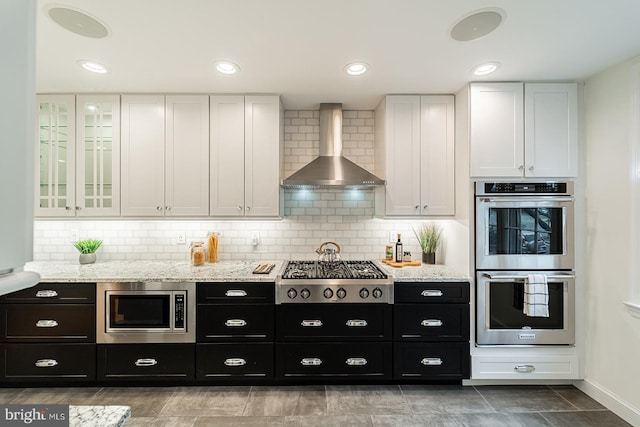 kitchen featuring white cabinets, stainless steel appliances, wall chimney range hood, and dark cabinets