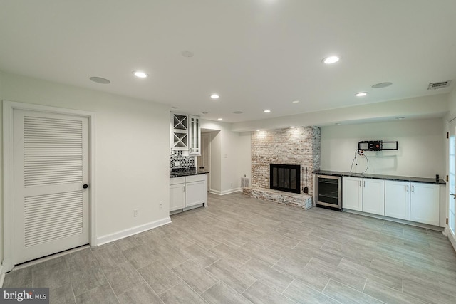 unfurnished living room with visible vents, beverage cooler, a dry bar, a stone fireplace, and recessed lighting