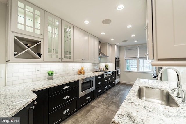 kitchen with a sink, appliances with stainless steel finishes, white cabinetry, wall chimney range hood, and dark cabinets