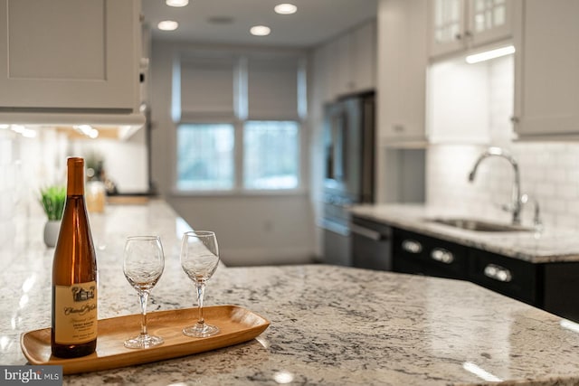 kitchen featuring a sink, fridge, light stone counters, and backsplash