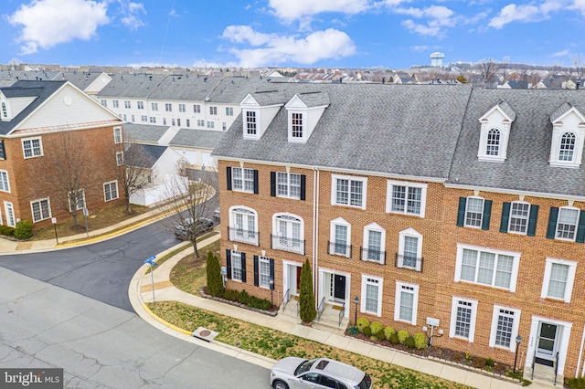 townhome / multi-family property featuring brick siding, a residential view, and a shingled roof