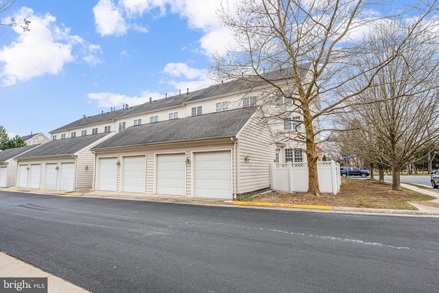 view of front of home featuring community garages, a residential view, roof with shingles, and fence