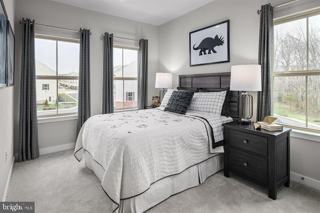 bedroom featuring multiple windows, light colored carpet, and baseboards