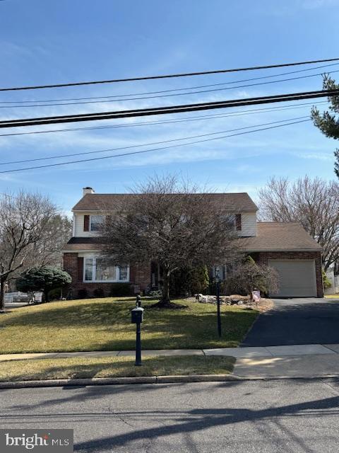 view of front facade with aphalt driveway, an attached garage, brick siding, and a front yard