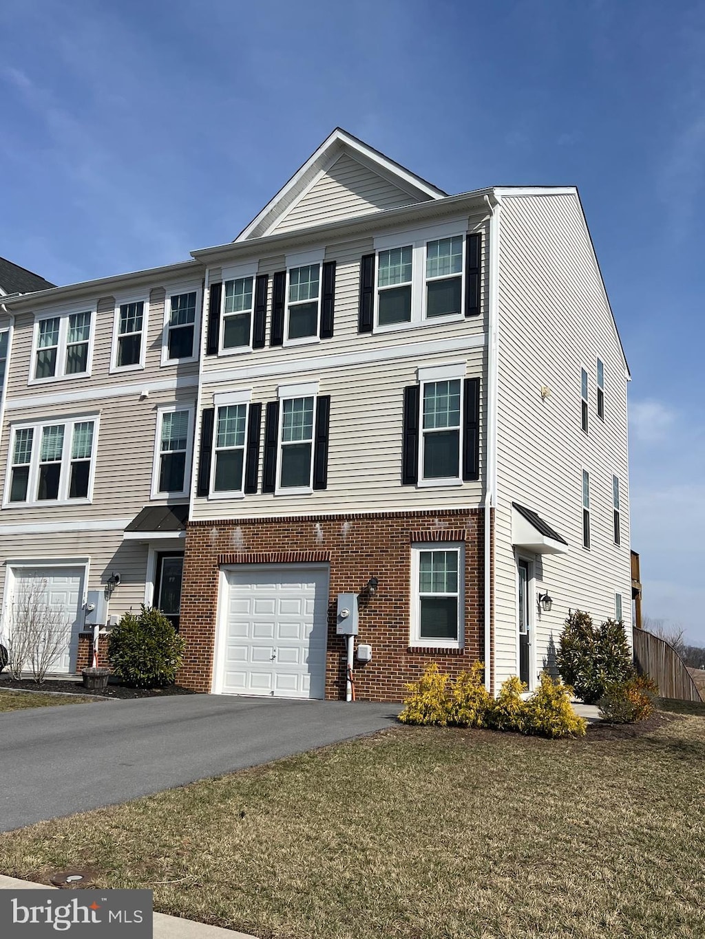 view of property featuring a front lawn, an attached garage, brick siding, and driveway