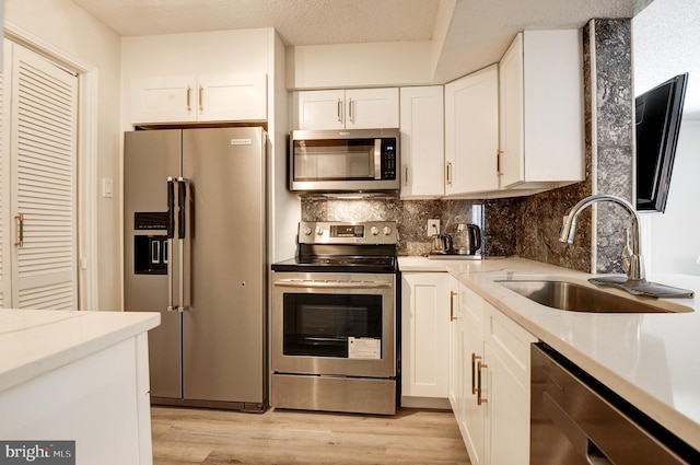 kitchen featuring white cabinets, stainless steel appliances, light wood-type flooring, and a sink