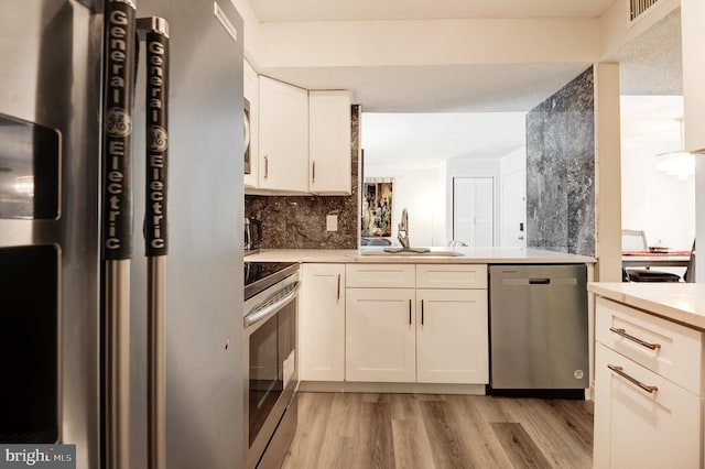 kitchen featuring a sink, decorative backsplash, stainless steel appliances, white cabinets, and light wood-style floors