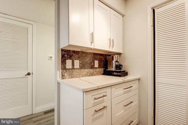 kitchen with light wood-style flooring, backsplash, baseboards, white cabinets, and light stone countertops