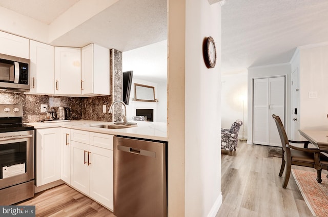 kitchen featuring tasteful backsplash, appliances with stainless steel finishes, light wood-style floors, white cabinets, and a sink