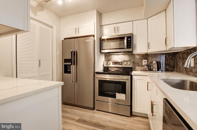 kitchen with light wood-type flooring, decorative backsplash, stainless steel appliances, white cabinetry, and a sink