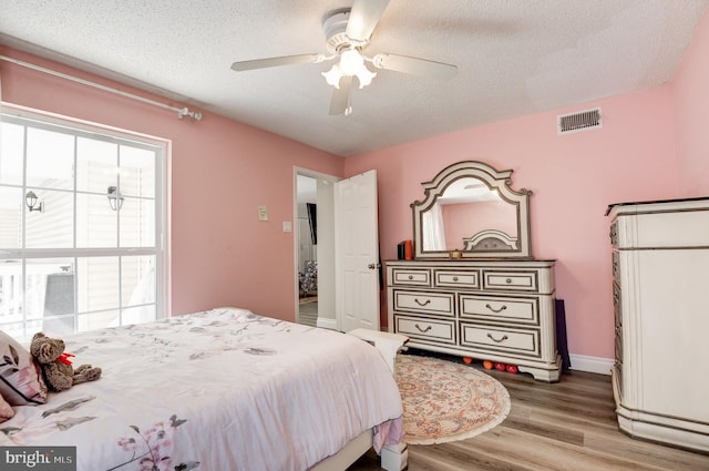 bedroom featuring visible vents, multiple windows, a textured ceiling, and wood finished floors