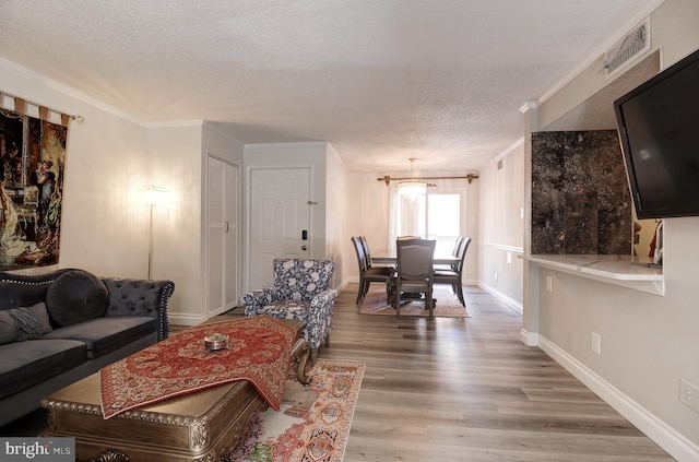 living room featuring visible vents, crown molding, baseboards, wood finished floors, and a textured ceiling