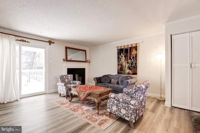 living area with crown molding, a fireplace, light wood-type flooring, and a textured ceiling