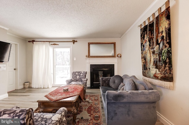 living area featuring baseboards, light wood-style flooring, a fireplace, ornamental molding, and a textured ceiling