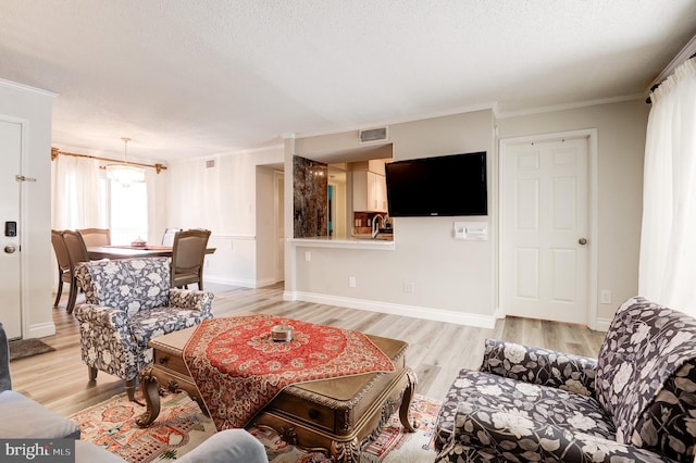 living area featuring baseboards, visible vents, light wood finished floors, ornamental molding, and a textured ceiling