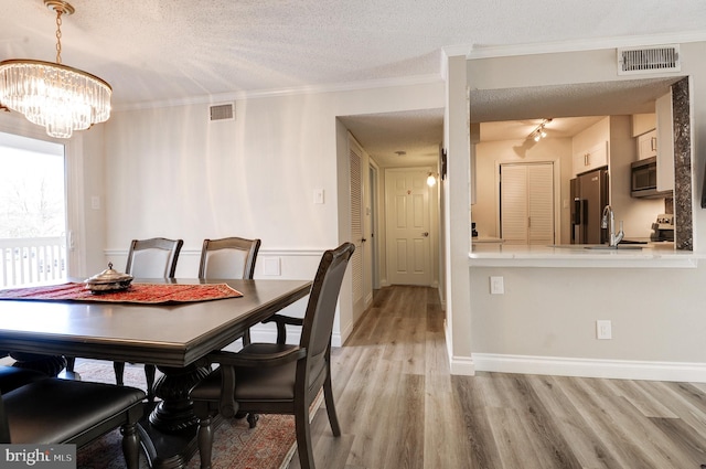 dining space featuring light wood-style floors, visible vents, a textured ceiling, and ornamental molding