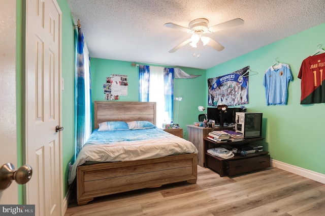 bedroom with a ceiling fan, wood finished floors, baseboards, and a textured ceiling