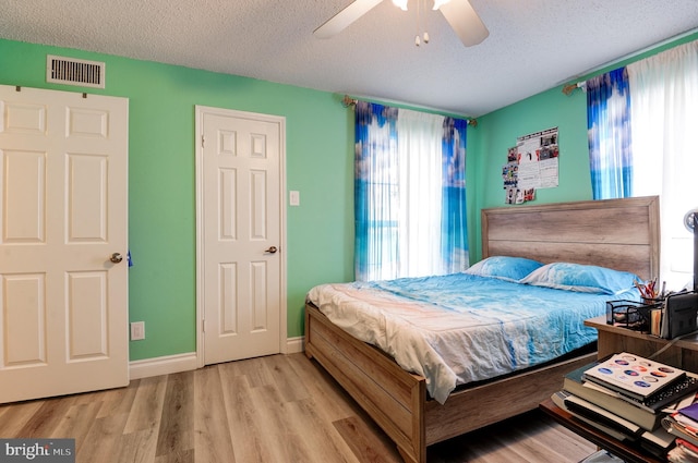 bedroom with visible vents, a textured ceiling, wood finished floors, baseboards, and ceiling fan