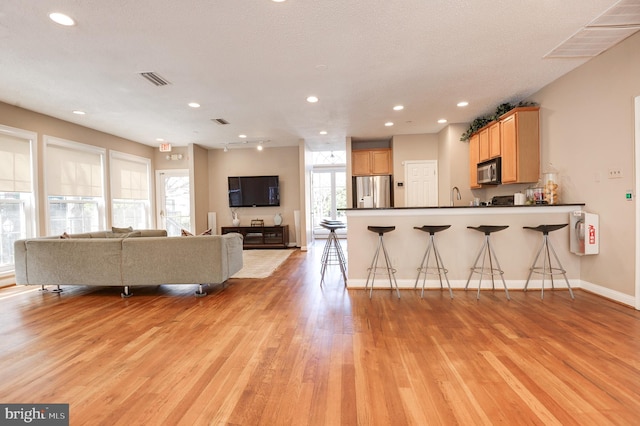 kitchen featuring a peninsula, stainless steel fridge with ice dispenser, light wood-style floors, dark countertops, and open floor plan