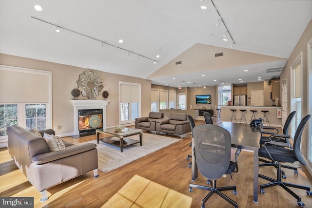 living room with a glass covered fireplace, high vaulted ceiling, visible vents, and wood finished floors