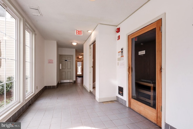 hall with visible vents, baseboards, and light tile patterned flooring