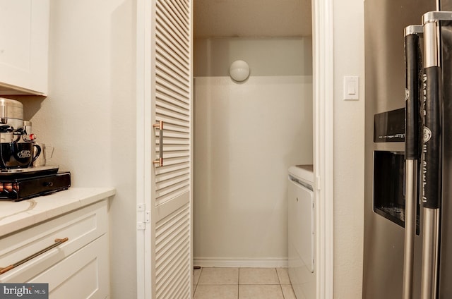 interior space with light tile patterned floors, washer / clothes dryer, stainless steel refrigerator with ice dispenser, and white cabinetry