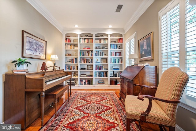sitting room with crown molding, wood finished floors, visible vents, and built in shelves