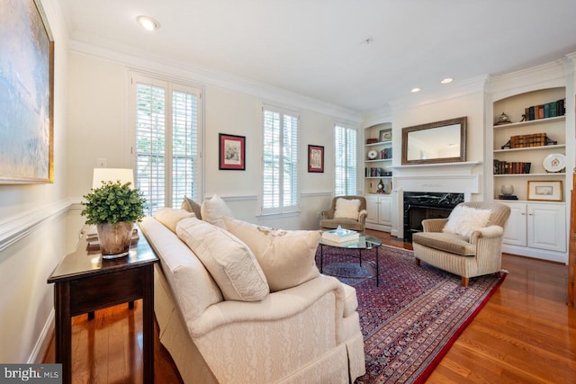 living room featuring crown molding, built in shelves, wood finished floors, and a fireplace