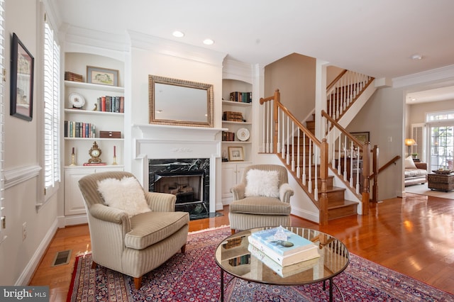 living room with a high end fireplace, stairway, light wood finished floors, and visible vents