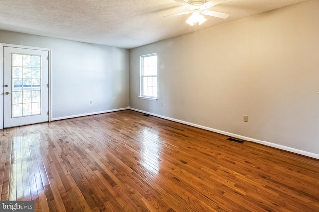 unfurnished room with visible vents, a textured ceiling, dark wood finished floors, baseboards, and ceiling fan