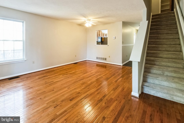 unfurnished living room with hardwood / wood-style floors, stairway, baseboards, and ceiling fan