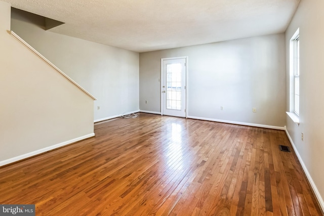 spare room with hardwood / wood-style floors, visible vents, baseboards, and a textured ceiling