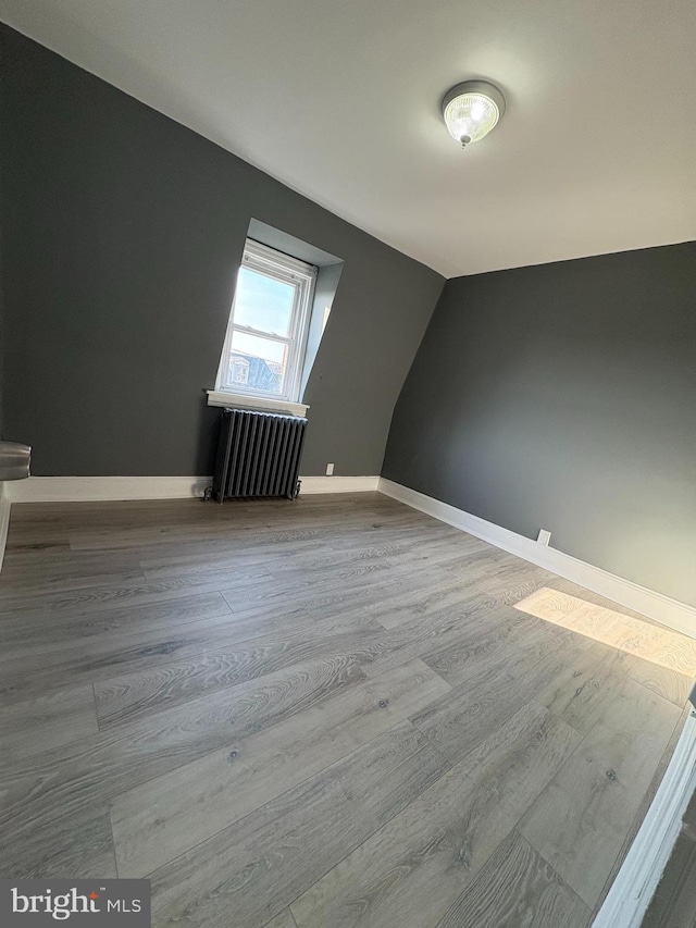 additional living space featuring baseboards, lofted ceiling, radiator, and wood finished floors