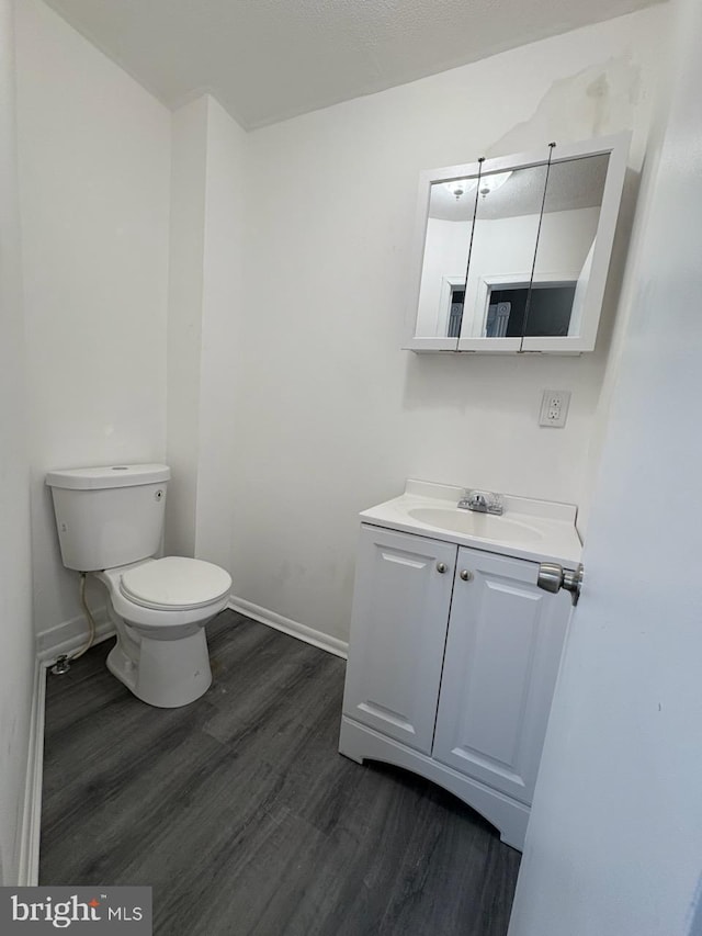 bathroom with vanity, toilet, wood finished floors, and baseboards