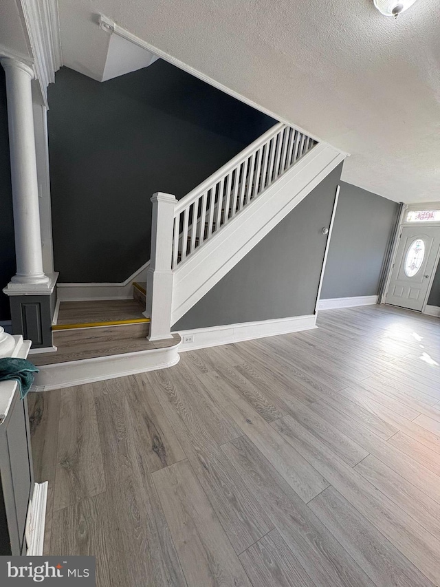 interior space featuring stairs, decorative columns, wood finished floors, and a textured ceiling