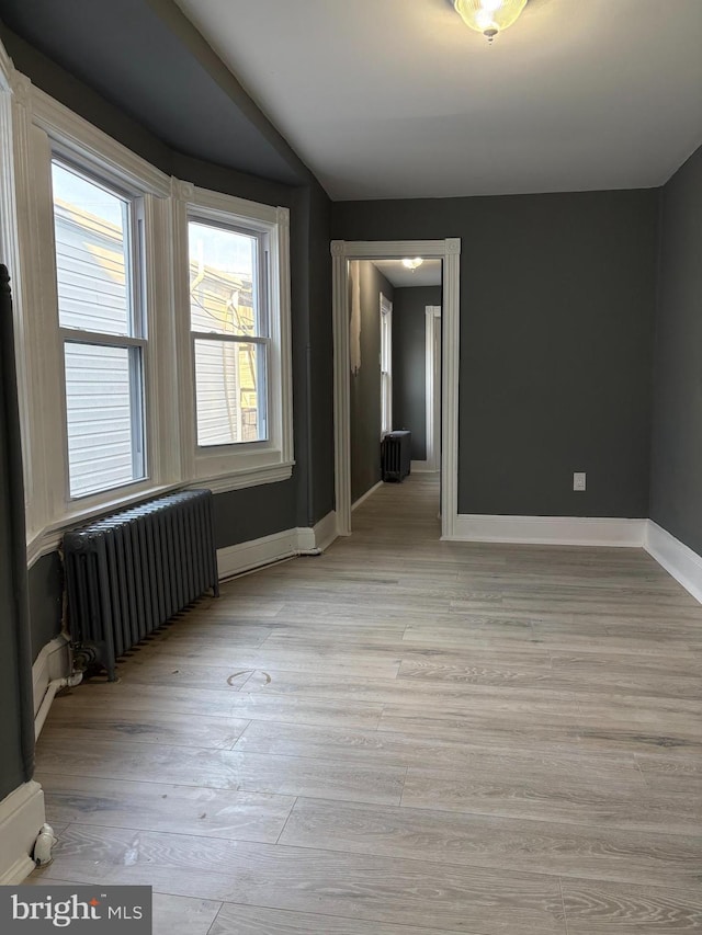 unfurnished room with baseboards, radiator heating unit, and light wood finished floors