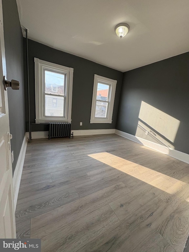 unfurnished room featuring a wealth of natural light, baseboards, wood finished floors, and radiator heating unit