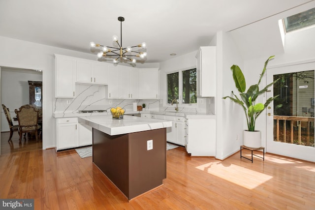 kitchen featuring light wood-type flooring, a kitchen island, light countertops, white cabinetry, and tasteful backsplash