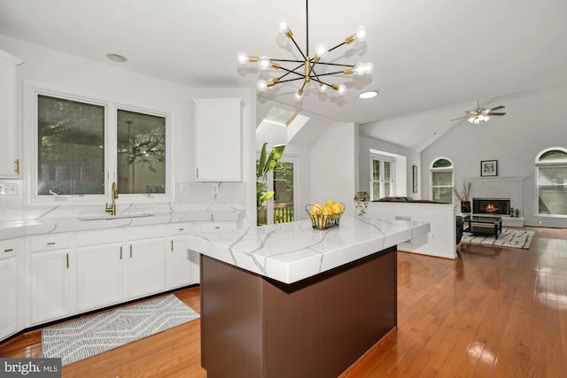 kitchen featuring a sink, a lit fireplace, lofted ceiling, white cabinetry, and wood-type flooring