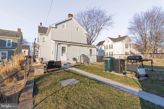 back of house featuring a yard, entry steps, a chimney, and a fenced backyard