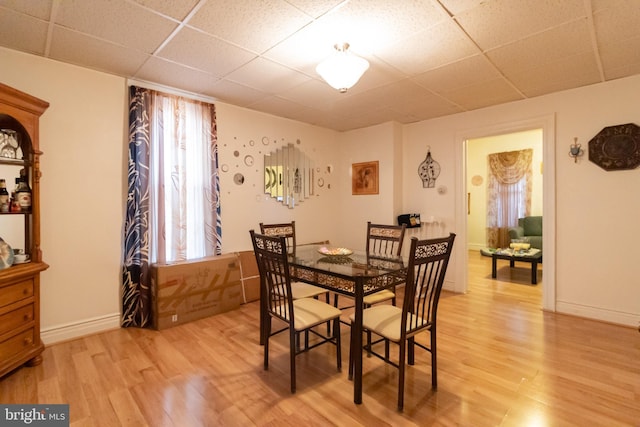 dining room featuring light wood-style flooring, a paneled ceiling, and baseboards