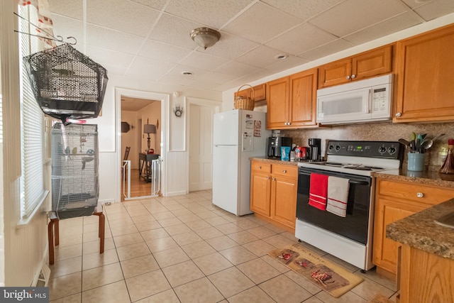 kitchen featuring white appliances, light tile patterned flooring, a drop ceiling, brown cabinets, and backsplash