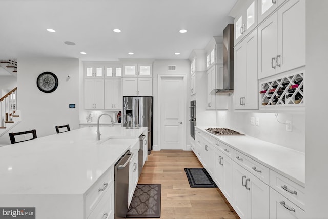 kitchen featuring visible vents, light wood-style flooring, light countertops, and wall chimney range hood