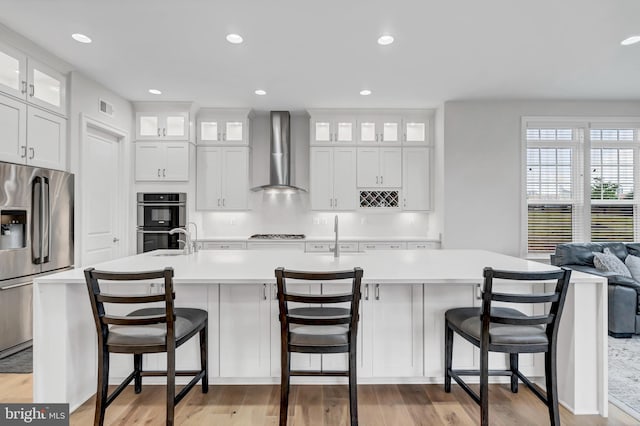 kitchen with visible vents, a kitchen island with sink, appliances with stainless steel finishes, wall chimney exhaust hood, and light countertops