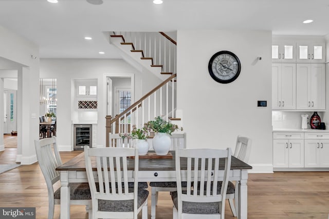 dining room featuring beverage cooler, baseboards, light wood finished floors, recessed lighting, and stairs