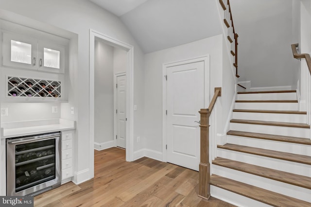 bar featuring beverage cooler, stairs, lofted ceiling, light wood-style flooring, and a bar