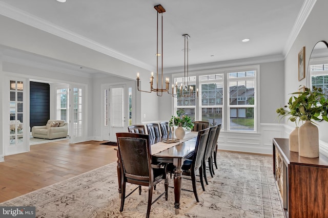 dining area featuring light wood-style flooring, ornamental molding, wainscoting, a decorative wall, and a chandelier