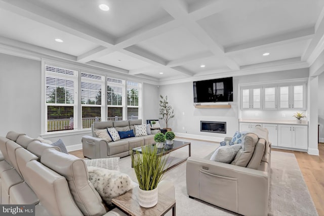 living area with light wood finished floors, baseboards, beamed ceiling, a glass covered fireplace, and coffered ceiling